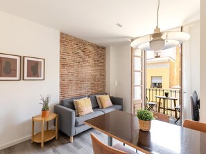 Un salon moderne avec un mur d’accent en briques, un canapé gris agrémenté de coussins à rayures, une table basse en bois et un balcon doté d’une rambarde en métal.