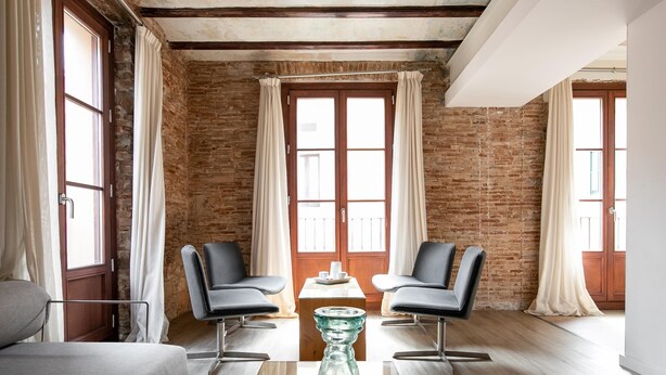 A modern room with a brick wall, two leather chairs, a glass coffee table, and a sofa.