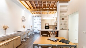 A modern kitchen with wooden beams, white cabinetry, and a dining area with a wooden table and chairs.