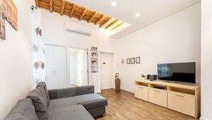 A modern living room with a grey sectional sofa, wooden flooring, a flat-screen TV on a wooden TV stand, and a ceiling with exposed beams.