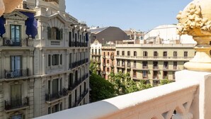 A balcony with ornate balustrades overlooking a cityscape with multi-story buildings.