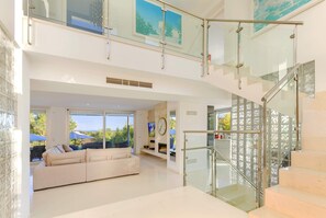 A modern interior with a glass staircase, a white sofa, and a view of the outdoors. - Villa Sol (Pollensa)