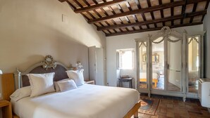 Een slaapkamer met een houten bed, witte beddengoed, een grote spiegel en een betegelde vloer.