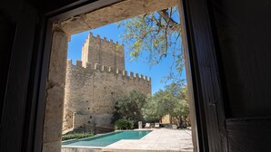 Door een deuropening zicht op een binnentuin met een zwembad, stenen trappen en een historisch kasteel op de achtergrond.