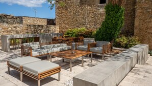 Een terras met stenen muren, een houten tafel en comfortabele zitplaatsen.