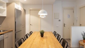 A modern kitchen with a wooden dining table, black chairs, a stainless steel refrigerator, and a pendant light. - DELUXE THREE BEDROOM APARTMENT (Barcelona)