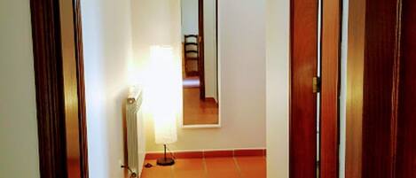 Un pasillo estrecho con suelo de baldosas, puertas de madera y un radiador.