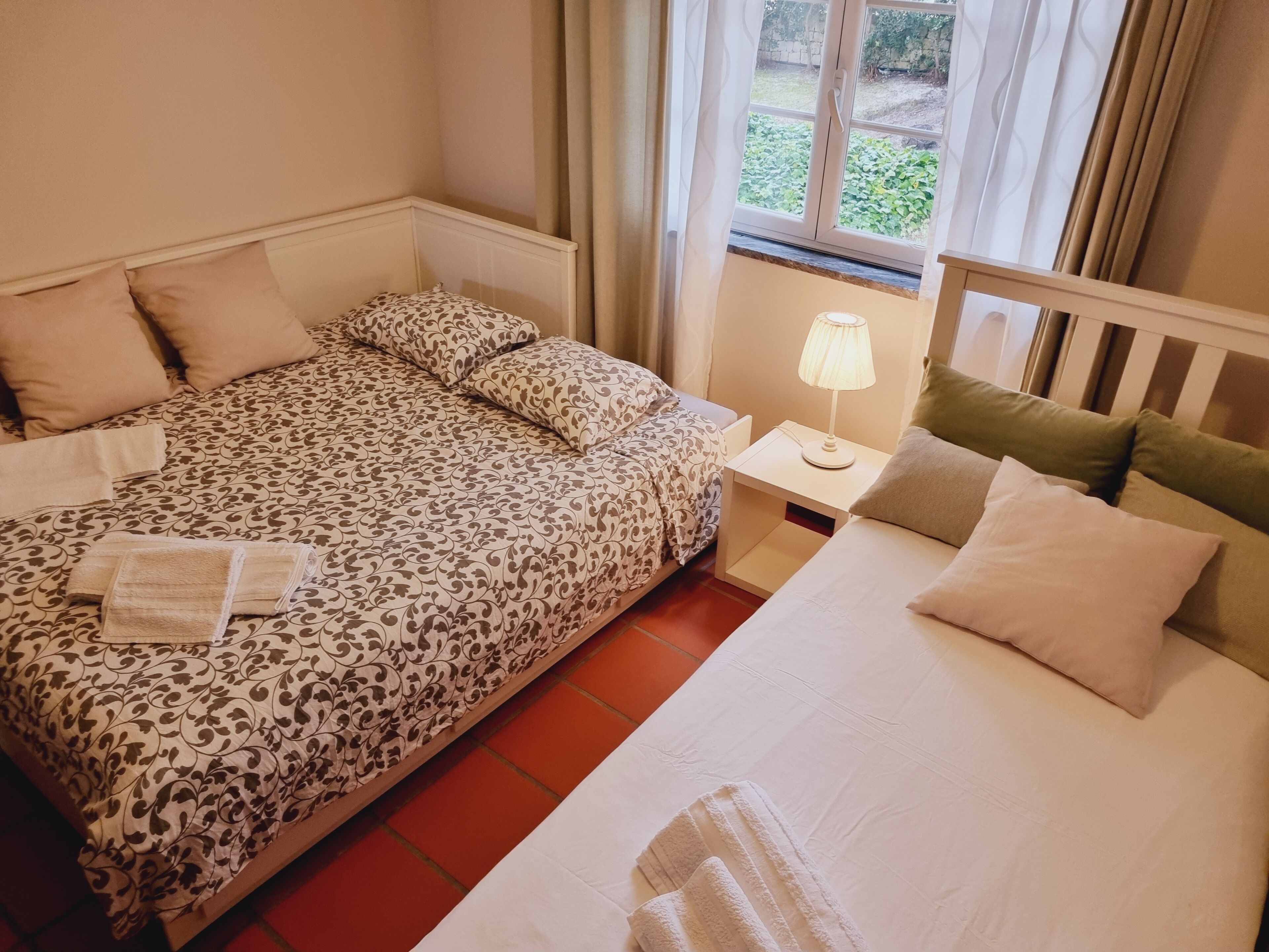 Et hotelværelse med en seng, et natbord, en lampe og et vindue med gardiner.