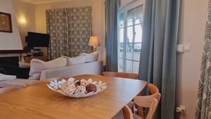 A dining table with a basket of food, a sofa, a television, and a window with curtains. - Obidos - Resort 5 * - Praia D'El Rey - Surf Golf & Beach - 2 bedroom apartment (Amoreira)