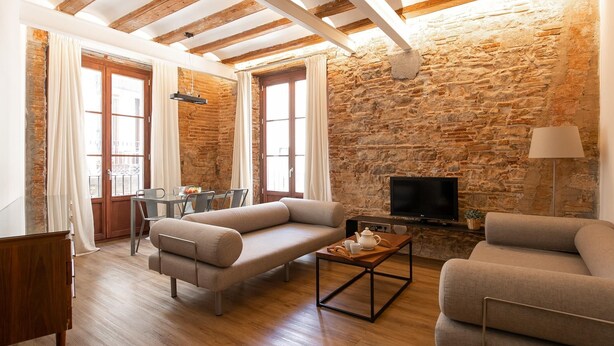 A cozy living room with a stone wall, wooden beams, a sofa, a coffee table, and a TV.