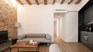 A modern living room with a stone wall, a grey sofa, a wooden coffee table with a tray, and a kitchen area with dark cabinets and appliances.