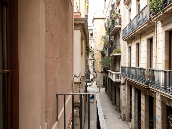 Une ruelle étroite en milieu urbain, bordée de bâtiments des deux côtés, avec des balcons ornés de plantes et un chemin piétonnier.