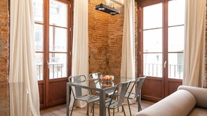 A dining area with a glass table and chairs, a stone wall, and large windows with curtains.