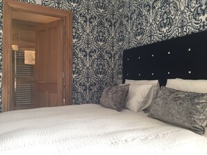 A bedroom with a patterned wallpaper, a wooden door, a bed with white bedding, and a dark headboard.