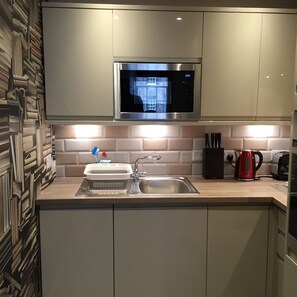 A modern kitchen with a stainless steel microwave, a sink, and a kettle.