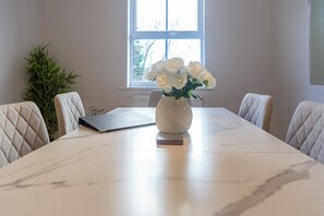 A conference table with a vase of white flowers, a laptop, and a plant in a room with a window.