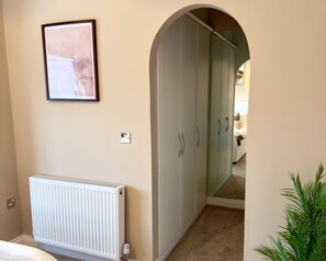 A hallway with a radiator, a framed picture on the wall, and a closet with a mirror.