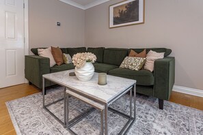 A living room with a green sofa, a white vase with flowers, and a marble coffee table.
