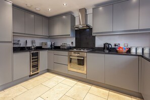 A modern kitchen with grey cabinetry, a stainless steel range hood, a built-in oven, and a black countertop.