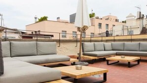 An outdoor seating area with a sofa and tables, a white umbrella, and a brick floor.