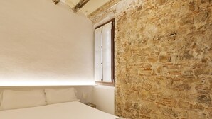 A bedroom with a large bed, white linens, a stone wall, and a window.