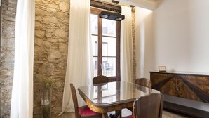 A dining area with a glass table, wooden chairs with red cushions, a stone wall, and a wooden cabinet.