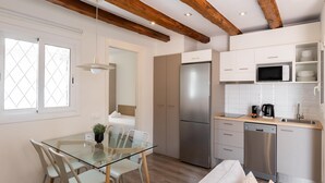A modern kitchen with a glass dining table, white chairs, a stainless steel refrigerator, and a microwave. - Penthouse Apartment with terrace (Barcelona)