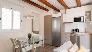 A modern kitchen with a stainless steel refrigerator, microwave, and dishwasher. There is a dining area with a glass table and chairs, and a sofa with patterned cushions. - Penthouse Apartment with terrace (Barcelona)
