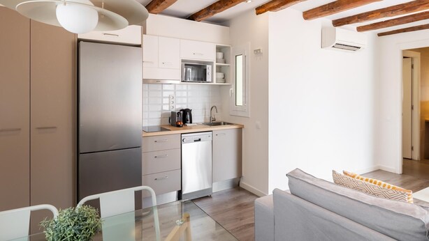 A modern kitchen with wooden beams, white cabinetry, and a glass dining table. - Penthouse Apartment with terrace (Barcelona)