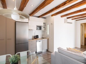 Una cocina moderna con vigas de madera, armarios blancos y una mesa de comedor de vidrio.