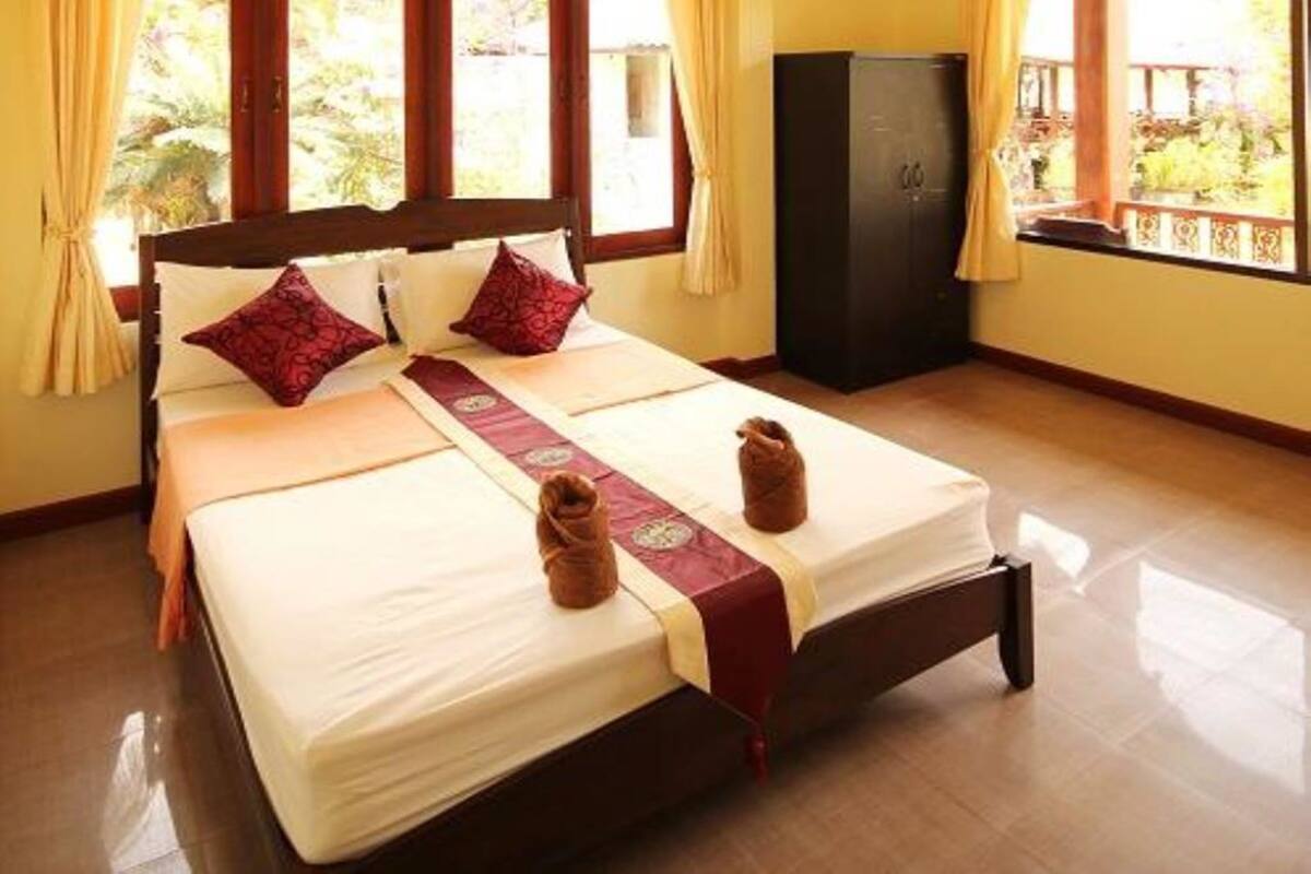 Una cama bien hecha con una colcha roja y blanca, dos almohadas y dos toallas sobre la cama.