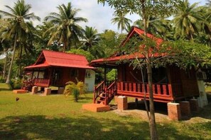 Ein Bungalow mit rotem Dach und Backsteinfundament, umgeben von Palmen und viel Grün.