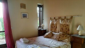 A neatly made bed with floral bedding, a bedside table with a lamp, and a window with curtains. - 2 bedrooms, large pool, stunning views of San Gimignano, Tuscany, private garden (San Gimignano, Tuscany)