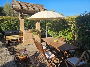 An outdoor patio with a wooden table and chairs, a grill, and a pergola with an umbrella.