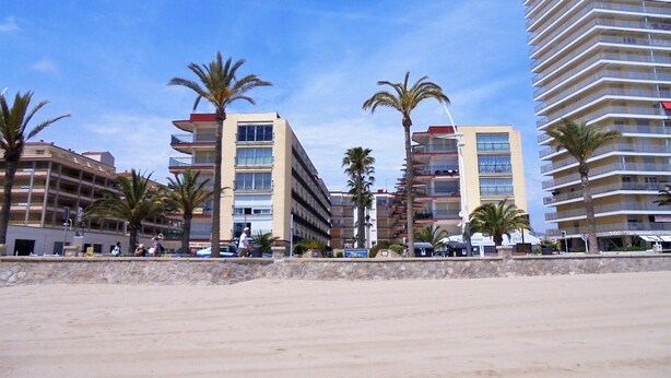 Un hôtel situé en bord de mer, avec plusieurs étages, des palmiers et un ciel d’un bleu éclatant.