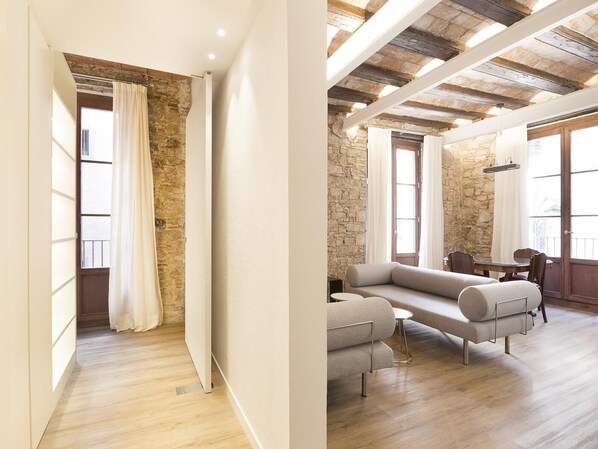A modern living room with a stone wall, wooden ceiling beams, a sofa, and a dining table. - Superior Deluxe One Bedroom Apartment (Barcelona)