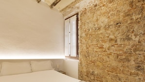 A bedroom with a large bed, white linens, a stone wall, and a window. - Superior Deluxe One Bedroom Apartment (Barcelona)