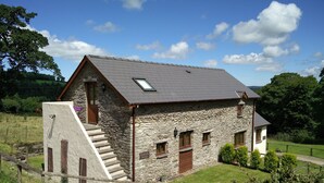 A stone farmhouse with a sloped roof, a staircase leading to the entrance, and a small garden area. - Fantastic couples escape to the country. Close to the coast in peaceful location (Boncath)