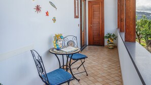 Ein schmaler Balkon mit Fliesenboden, einer Holztür und einem kleinen Tisch mit Stühlen.