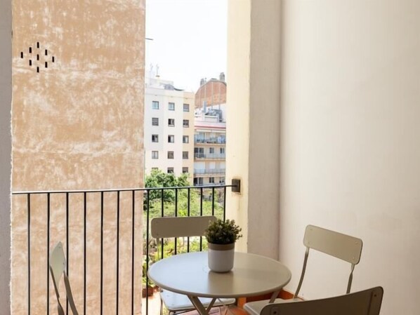 A balcony with a round table and two chairs, a potted plant, and a view of multi-story buildings.