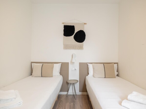 Une chambre avec deux lits, un petit tabouret et un objet fixé au mur.
