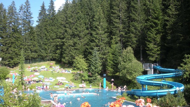 A swimming pool surrounded by a forest, with people sunbathing and swimming. - Hotel Garni Central (Kappl)
