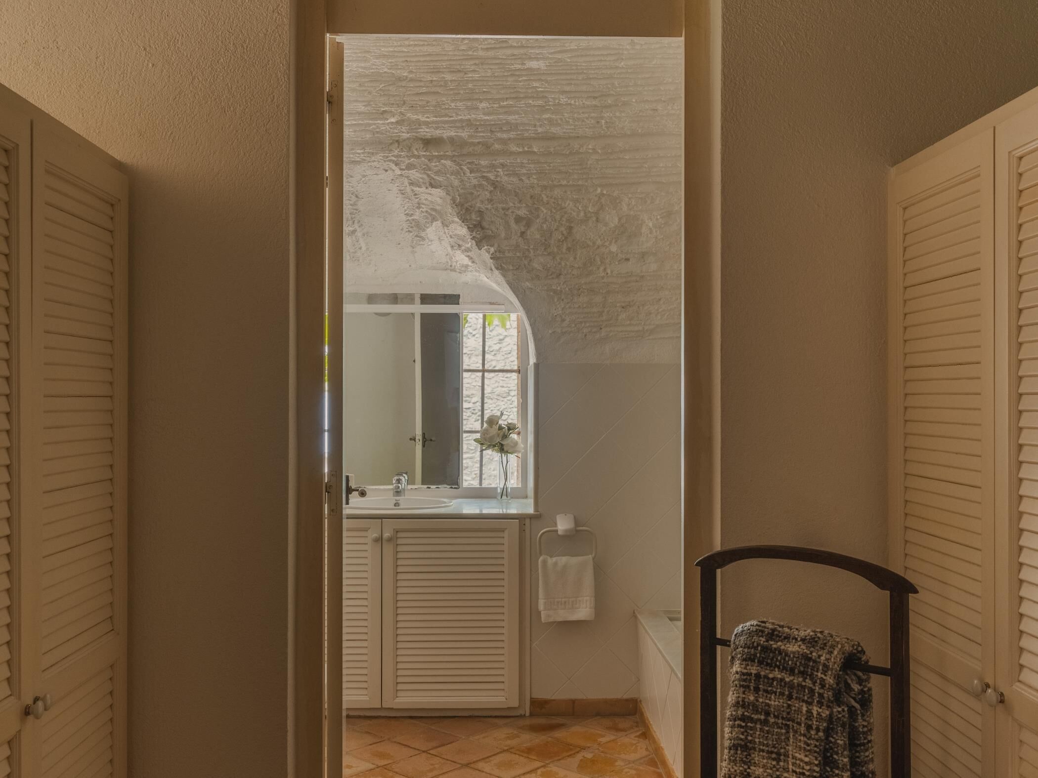 En smal hall med ett badrum som har ett handfat, en spegel och en handdukshängare.