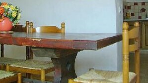 Una mesa de comedor con sillas, un jarrón de flores y una zona de cocina con armarios y un frutero.