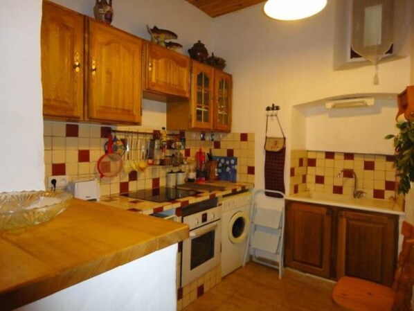 Cocina compacta con armarios de madera, salpicadero azulejado, lavadora y un lavamanos pequeño.