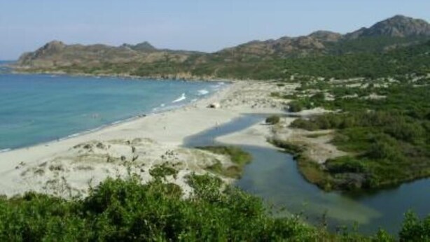 Un paisaje costero con una playa, un río y montañas al fondo.