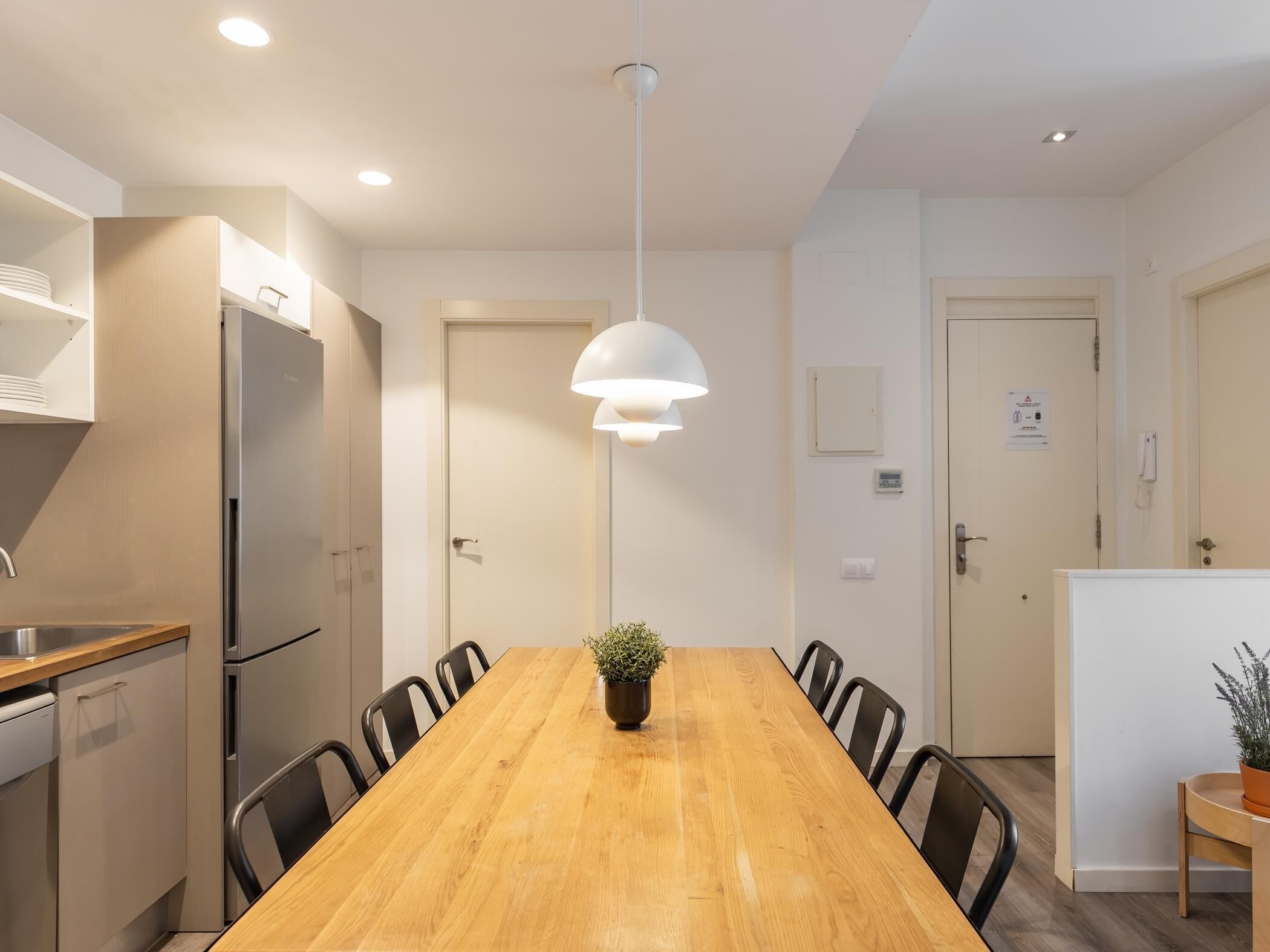 Una cocina moderna con una mesa de comedor de madera, sillas negras, un refrigerador de acero inoxidable y una lámpara colgante.