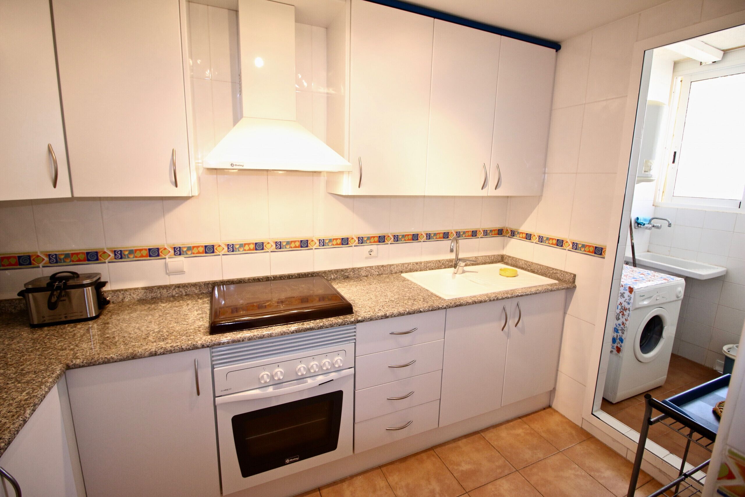 A kitchen with white cabinets, a stove, a sink, and a washing machine.