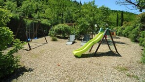 Ein Spielplatz mit Rutsche und Schaukeln, umgeben von Bäumen.