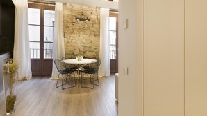A dining area with a stone wall, a round table with four chairs, and a hanging light fixture. - Deluxe One Bedroom Apartment (Barcelona)